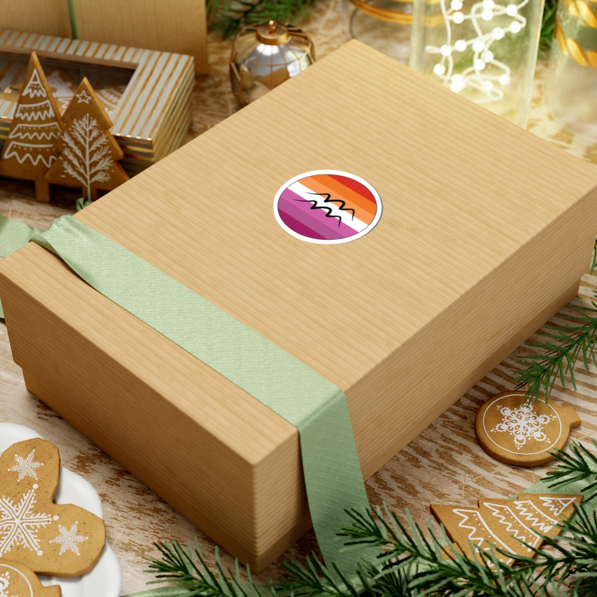 Gift box with a green ribbon on a festive background with cookies and Christmas decorations. Aquarius Lesbian pride sticker centered on the box.