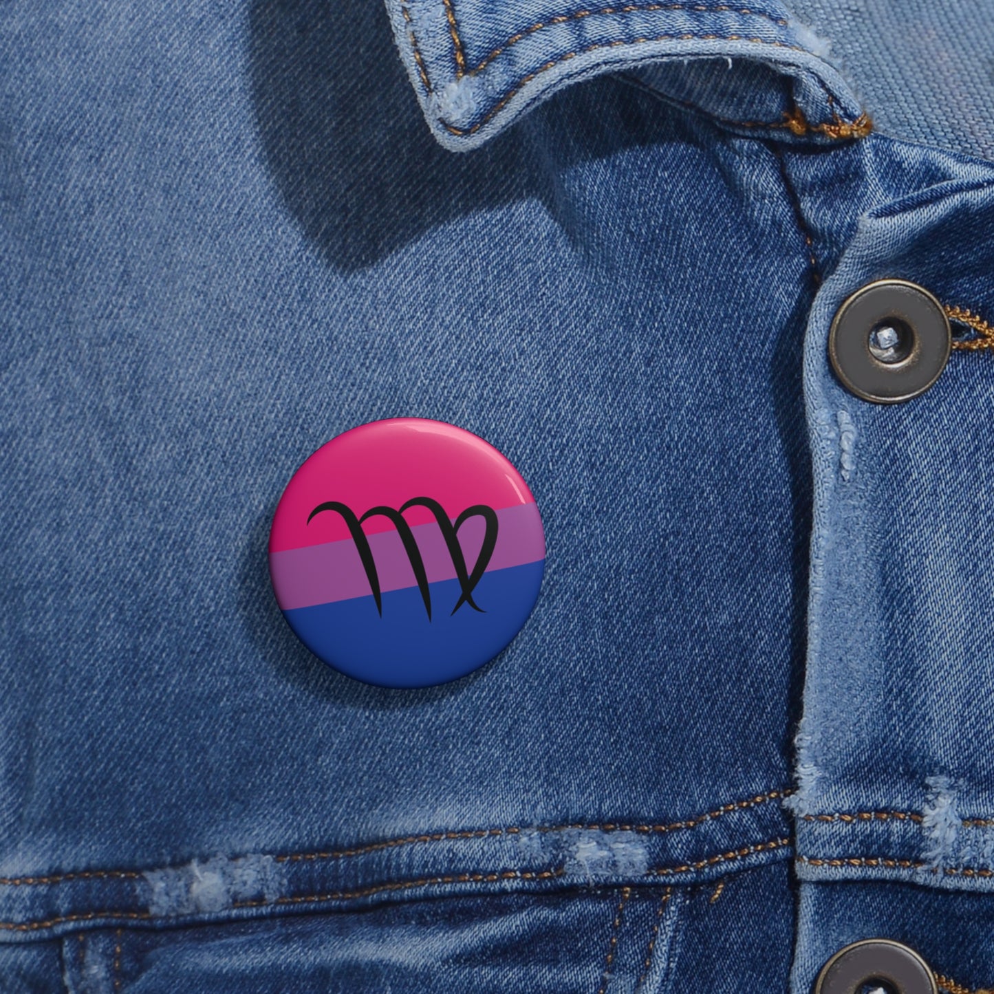 Close-up of a white circular pride button featuring the Virgo zodiac glyph centered over a bisexual pride flag background in pink, purple, and blue, attached to a blue denim jacket at the right chest with the button clearly visible.