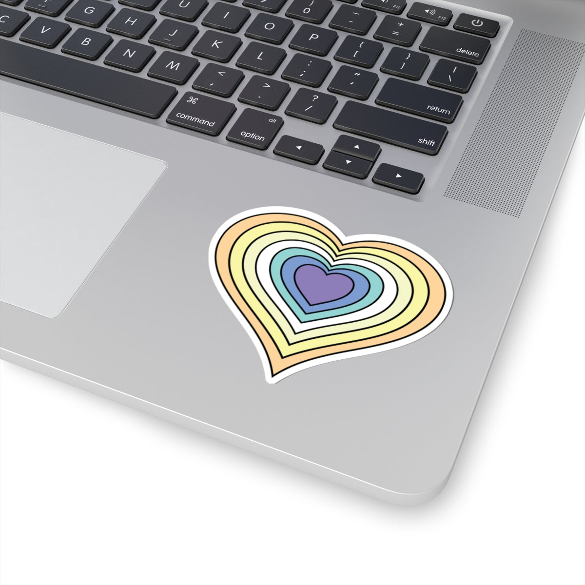 Close-up of the bottom right corner of a silver laptop featuring a 3 inch by 3 inch pride flag heart sticker in a Genderfaun flag style applied to the surface.