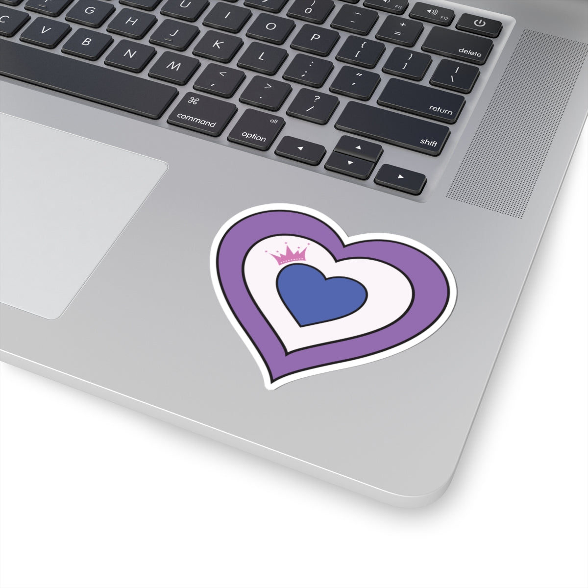 Close-up of the bottom right corner of a silver laptop featuring a 3 inches by 3 inches pride flag heart sticker in a Drag pride flag style applied to the surface.