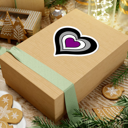 Gift box with a green ribbon on a festive background with cookies and Christmas decorations. Heart-shaped Asexual pride sticker centered on the box.