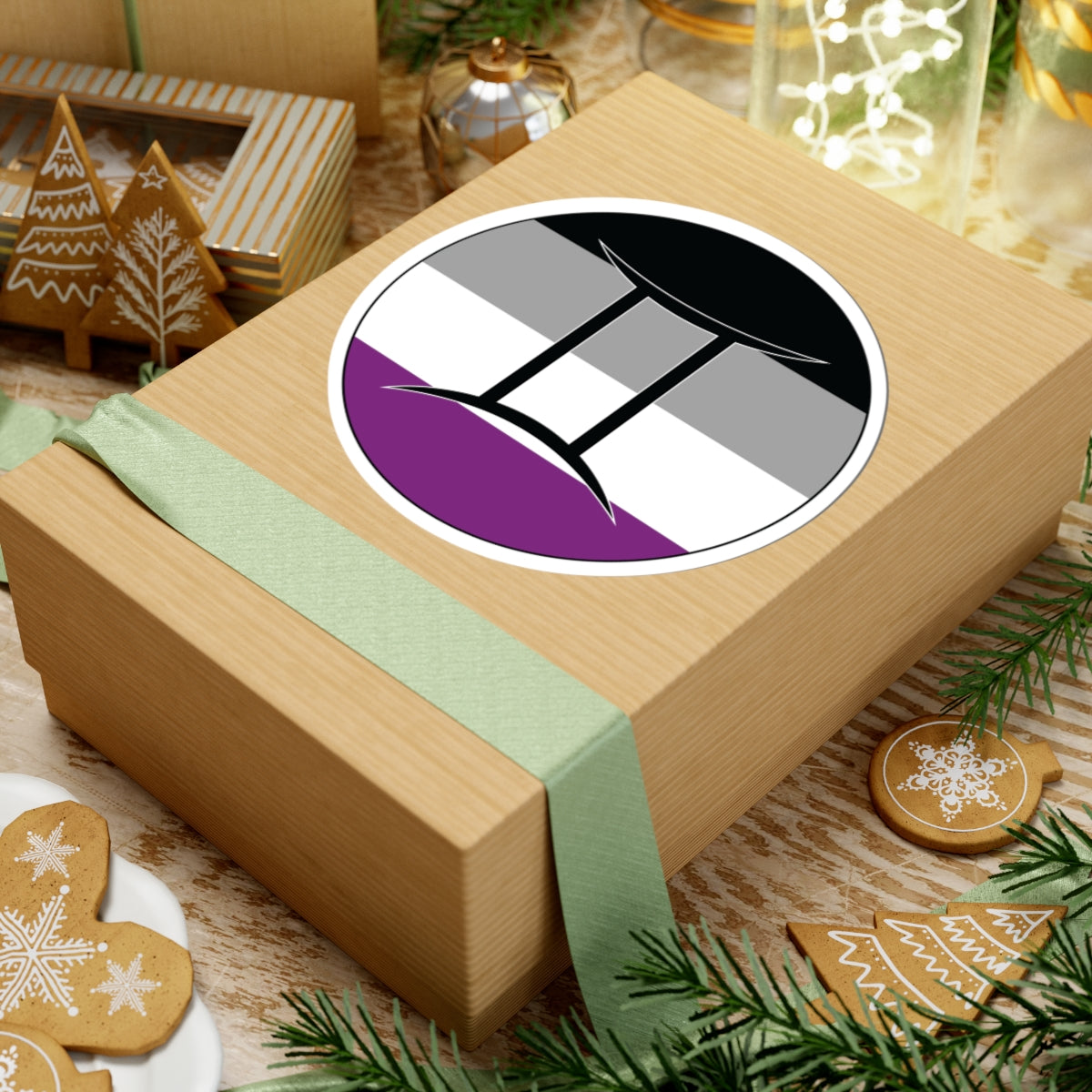 Gift box with a green ribbon on a festive background with cookies and Christmas decorations. Gemini Asexual pride sticker centered on the box.