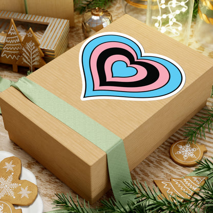 Gift box with a green ribbon on a festive background with cookies and Christmas decorations. Heart-shaped Transfeminine pride sticker centered on the box.