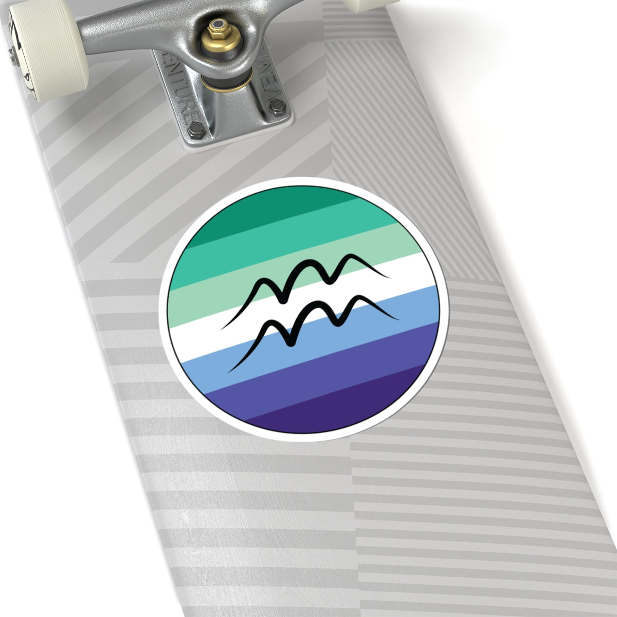 Close-up of the bottom of a silver skateboard featuring a 6 inch by 6 inch circular zodiac sticker with a centered Aquarius glyph on a Gay Men pride flag style background applied to the surface.