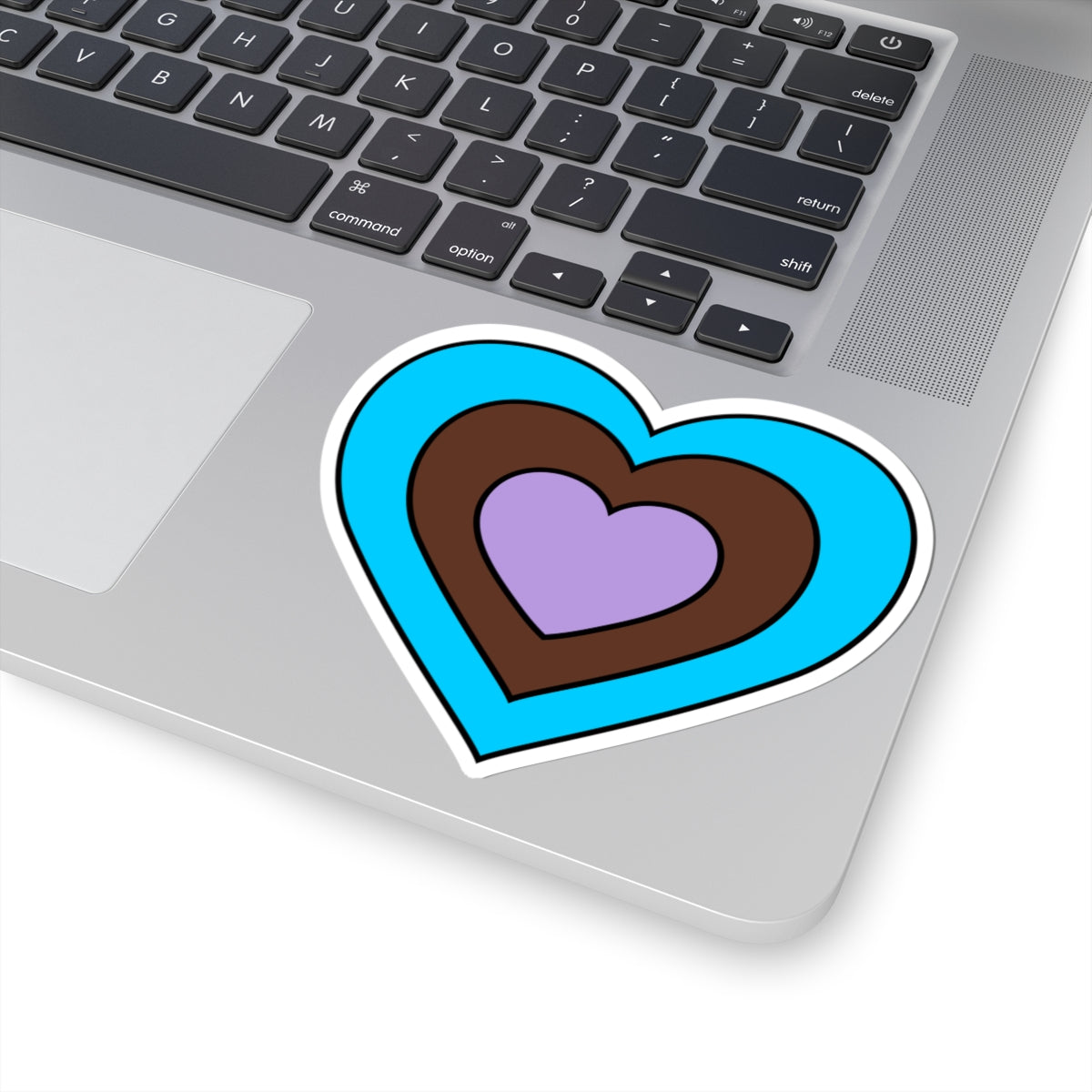 Close-up of the bottom right corner of a silver laptop featuring a 4 inch by 4 inch pride flag heart sticker in an Androsexual flag style applied to the surface.