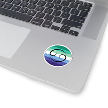 Close-up of the bottom right corner of a silver laptop featuring a 2 inch by 2 inch circular zodiac sticker with a centered Cancer glyph on a Gay Men pride flag style background applied to the surface.