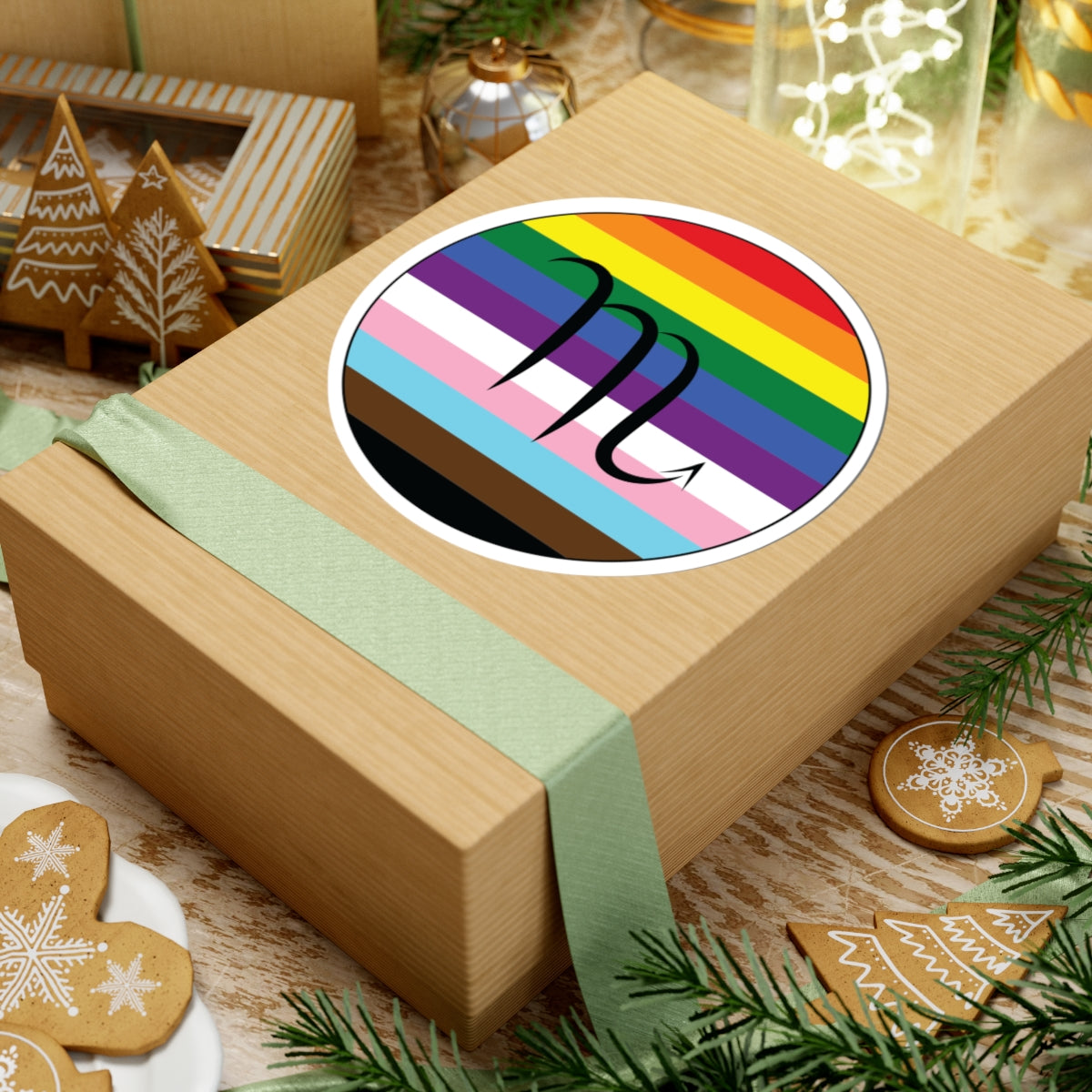 Gift box with a green ribbon on a festive background with cookies and Christmas decorations. Scorpio Progress pride sticker centered on the box.