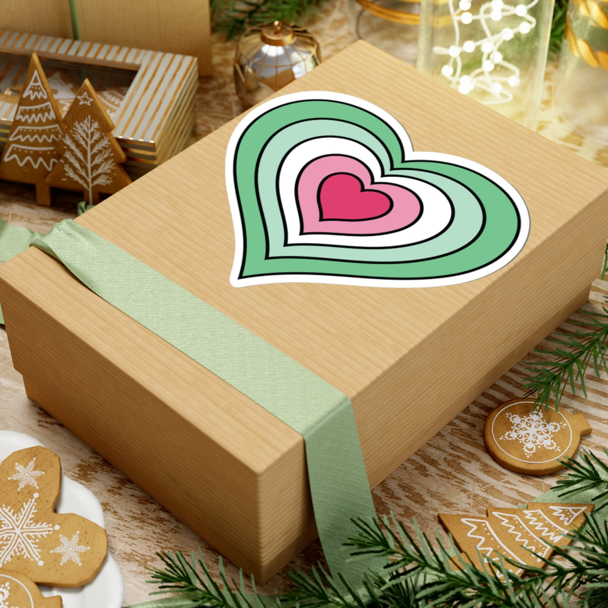 Gift box with a green ribbon on a festive background with cookies and Christmas decorations. Heart-shaped Abrosexual pride sticker centered on the box.