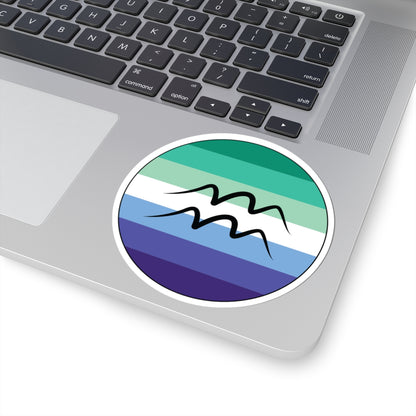 Close-up of the bottom right corner of a silver laptop featuring a 4 inch by 4 inch circular zodiac sticker with a centered Aquarius glyph on a Gay Men pride flag style background applied to the surface.