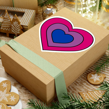 Gift box with a green ribbon on a festive background with cookies and Christmas decorations. Heart-shaped Bisexual pride sticker centered on the box.