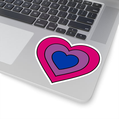 Close-up of the bottom right corner of a silver laptop featuring a 4 inch by 4 inch pride flag heart sticker in a Bisexual flag style applied to the surface.