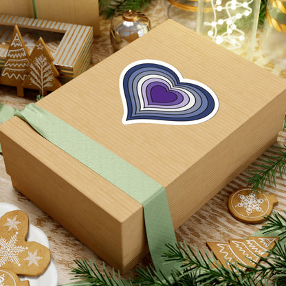 Gift box with a green ribbon on a festive background with cookies and Christmas decorations. Purple Butch pride heart sticker centered on the box.