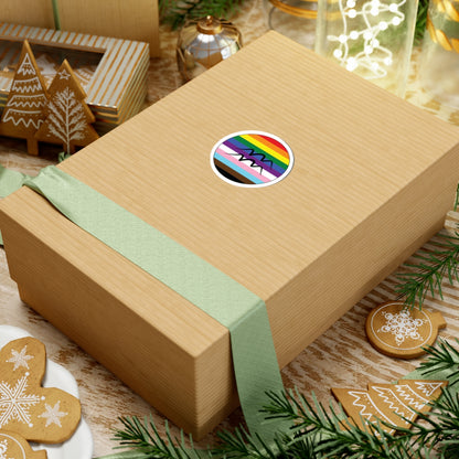 Gift box with a green ribbon on a festive background with cookies and Christmas decorations. Aquarius Progress pride sticker centered on the box.