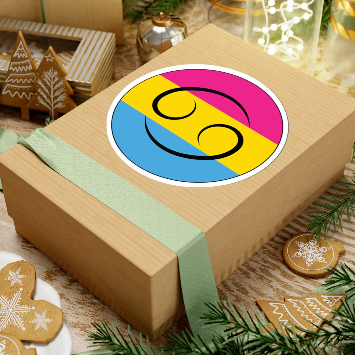 Gift box with a green ribbon on a festive background with cookies and Christmas decorations. Cancer Pansexual pride sticker centered on the box.
