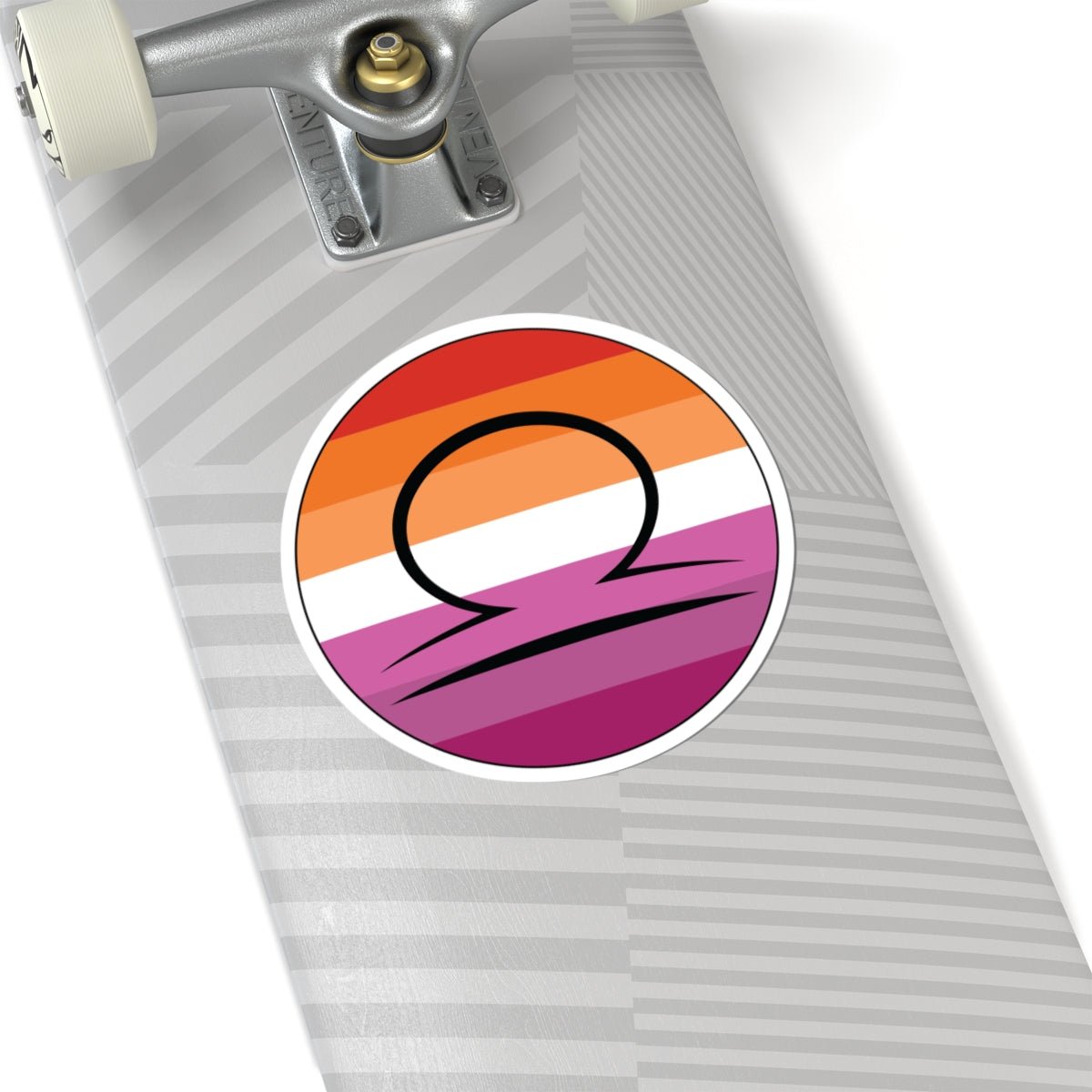 Close-up of the bottom right corner of a silver laptop featuring a 6 inch by 6 inch circular zodiac sticker with a centered Libra glyph on a Lesbian pride flag style background applied to the surface.