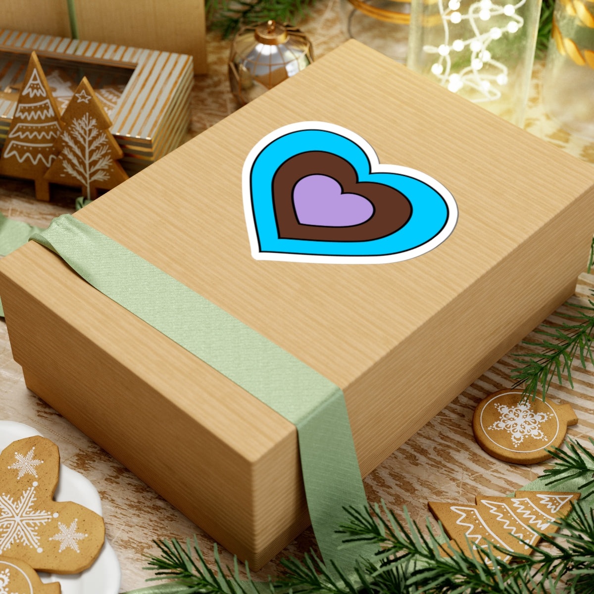 Gift box with a green ribbon on a festive background with cookies and Christmas decorations. Heart-shaped Androsexual pride sticker centered on the box.