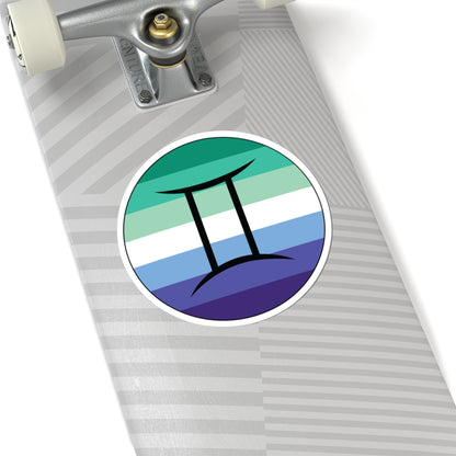 Close-up of the bottom of a silver skateboard featuring a 6 inch by 6 inch circular zodiac sticker with a centered Gemini glyph on a Gay Men pride flag style background applied to the surface.