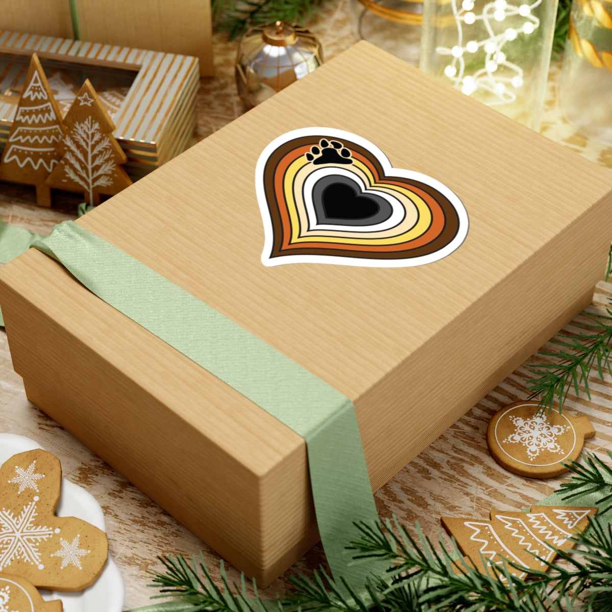 Gift box with a green ribbon on a festive background with cookies and Christmas decorations. Bear pride heart sticker centered on the box.