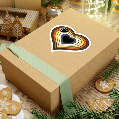 Gift box with a green ribbon on a festive background with cookies and Christmas decorations. Bear pride heart sticker centered on the box.