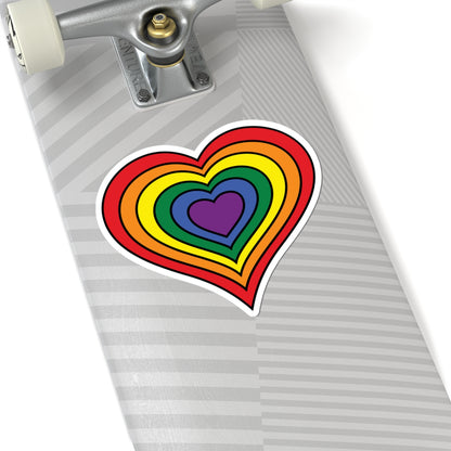 Close-up of the bottom of a silver skateboard featuring a 6 inch by 6 inch pride flag heart sticker in a rainbow pride flag style applied to the surface.