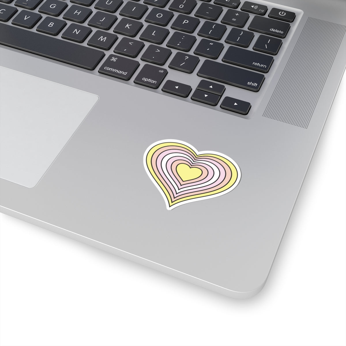 Close-up of the bottom right corner of a silver laptop featuring a 2 inch by 2 inch pride flag heart sticker in a Pangender flag style applied to the surface.
